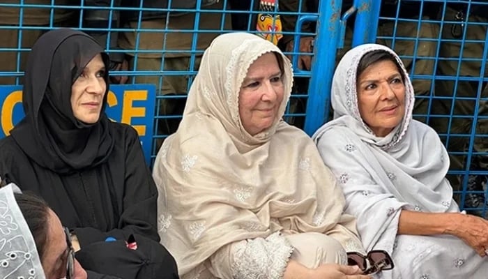 Three women seated beside a police vehicle, in a report on the MPO detention of Imran Khan's sisters
